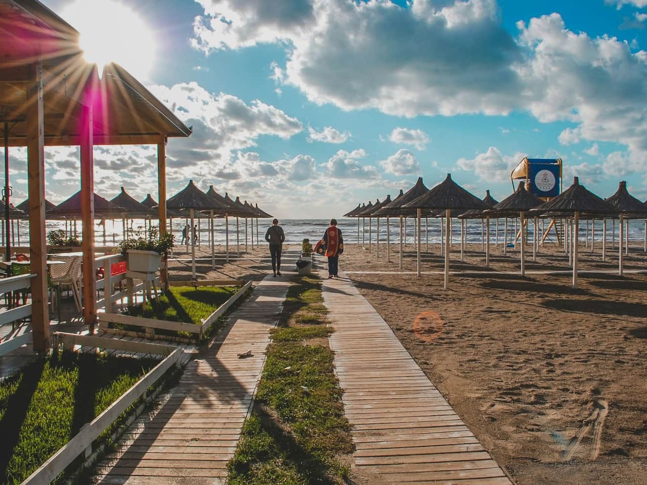 Albanian Riviera beach at golden hour — boardwalk leading toward parasols on the sand.